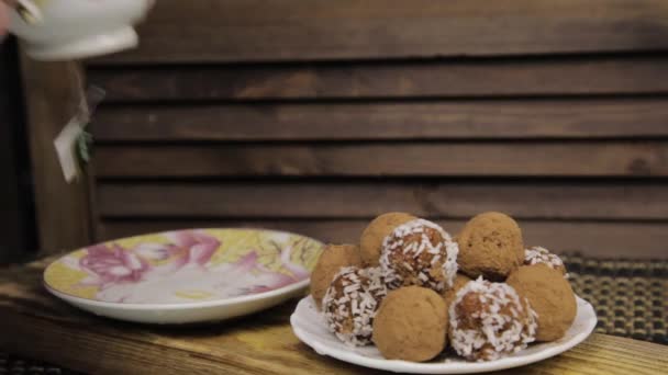 Chocolade snoepjes en thee op een houten tafel. Porselein thee set op een woodan achtergrond — Stockvideo