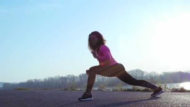 Спортсменка займається спортом на березі річки на сході сонця. повільний рух — стокове відео