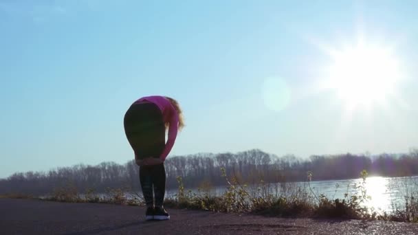 Die sportliche Frau treibt bei Sonnenaufgang Sport am Ufer des Flusses. Zeitlupe — Stockvideo