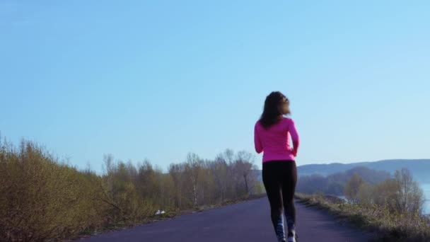 Sportive girl jogging along the river bank during sunrise or sunset. healthy lifestyle concept of athletic woman goes in for sports. slow motion — Stock Video