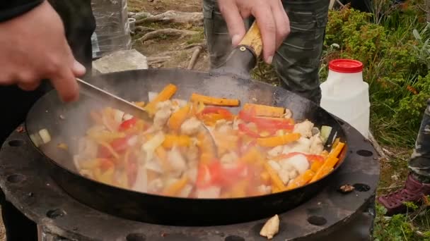 Cooking vegetables with meat outdoors . fried vegetables in a cauldron. vacation concepte. smoke rises slowly over the pan. slow motion. — Stock Video