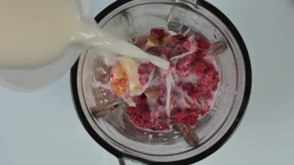 Jovem cozinhando um coquetel de frutas e bagas em um liquidificador. Derramando leite no liquidificador com framboesas. alimentação saudável e conceito de dieta — Vídeo de Stock