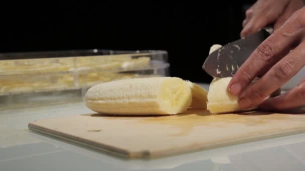 Vrouwen met behulp van keuken mes dia gesneden banaan op houten snijplank. Banaan snijden voor gedroogde vruchten — Stockvideo