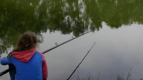 Χαριτωμένο έφηβος κορίτσι ψάρεμα στην όχθη του ποταμού στέκεται στην άμμο και κρατώντας ράβδος ψαρέματος. — Αρχείο Βίντεο