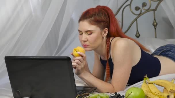 赤毛の女性は、ベッドに横たわっている間新鮮な果物を食べる。健康的な朝食。スローモーション — ストック動画