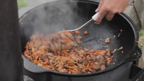 Cooking of pilaff with lamb, carrots and spices onions in a cauldron on a wood stove — Stock Video