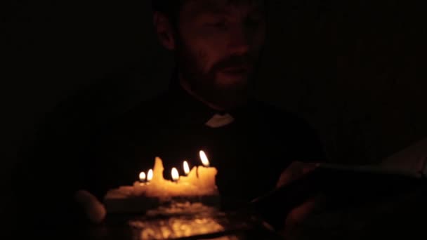 Католицький пастор запалює свічки і читає зі Святої Біблії в темряві — стокове відео