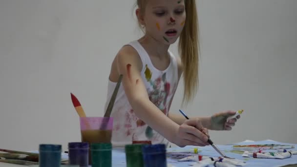 Uma colegial. Bonito pintor menina desenha sobre a mesa e sobre si mesmo em suas roupas. câmara lenta — Vídeo de Stock