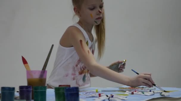 Pequeña colegiala. Lindo pintor niña dibuja en la mesa y en sí mismo en su ropa. cámara lenta — Vídeos de Stock