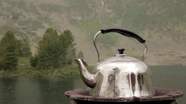 The iron kettle is boiling on the shore of a mountain lake. camping concepte — Stock Video