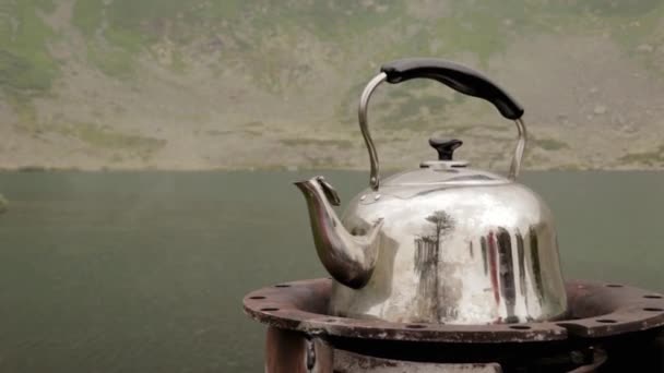 The iron kettle is boiling on the shore of a mountain lake. camping concepte — Stock Video