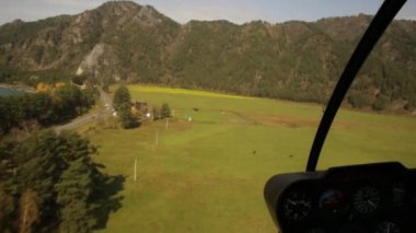 Helikopterin kokpitinden görüntü. Alçaktan uçan helikopter dağlık bir bölgede nehir yatağının üzerinden uçuyor.