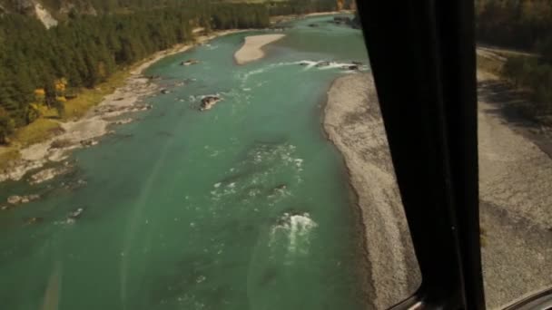 Вид из вертолетной кабины. Низколетящий вертолет пролетает над руслом реки в горной местности — стоковое видео
