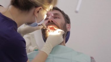 Kadın dişçi erkek hastaya diş tedavisi yapıyor. Dişçi anestezi iğnesi yapar. Kadın profesyonel doktor stomatolog iş başında.