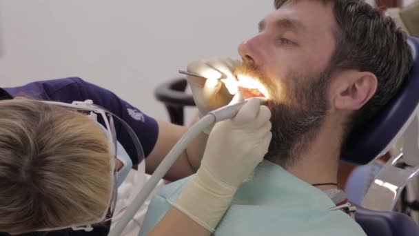 Dokter gigi wanita merawat gigi pasien pria. Ahli perut mengobati karies pada gigi pasien. Prosedur kebersihan mulut gigi di kedokteran gigi — Stok Video