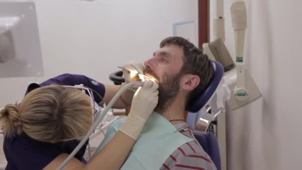 Η οδοντίατρος θεραπεύει έναν ασθενή στην οδοντιατρική κλινική. Οδοντιατρικός έλεγχος. Στοματολόγος αντιμετωπίζει τερηδόνα σε ασθενείς δόντια — Αρχείο Βίντεο
