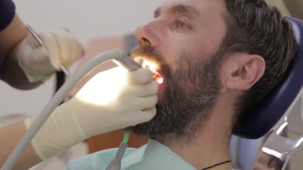 Dentystka leczy męskie zęby. Stomatolog leczy próchnicę zębów. Procedura higieny jamy ustnej w stomatologii — Wideo stockowe