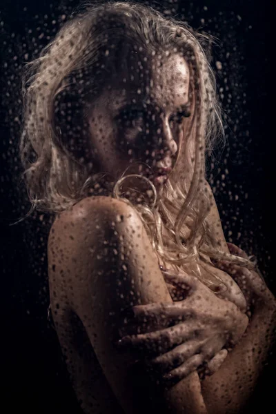 Beautyful blonde woman behind wet glass on a dark background, woman takes a shower — Stock Photo, Image