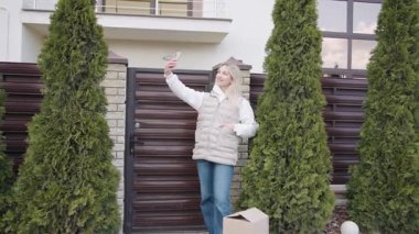 Yeşilliklerle çevrili bir evin girişinde selfie çeken bir kadın.