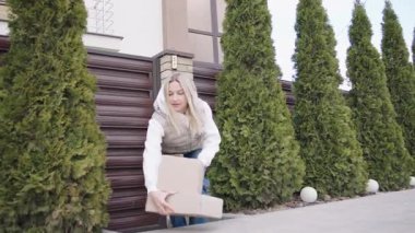 Dişi kurye, güpegündüz çevresi yeşilliklerle çevrili konut binasının dışına paket teslim ediyor.