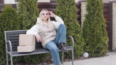 Kadın dışarıda güneşli bir günün tadını çıkarırken posta kutularıyla bankta oturuyor.