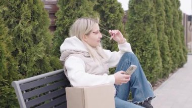 Kadın, yanında bir kutuyla parktaki bankta teslimatı beklerken mola veriyor.