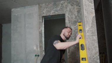 İçerideki bir inşaat projesinde çalışırken duvarların hizalanmasını sağlamak için bir seviye aracı kullanan adam