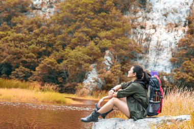 Uzun yürüyüşe çıkan kimse kadın muzaffer oturma sonbahar ormandaki nehir ve tatil kamp yakınındaki sakin hissediyorum. Seyahat kavramı.