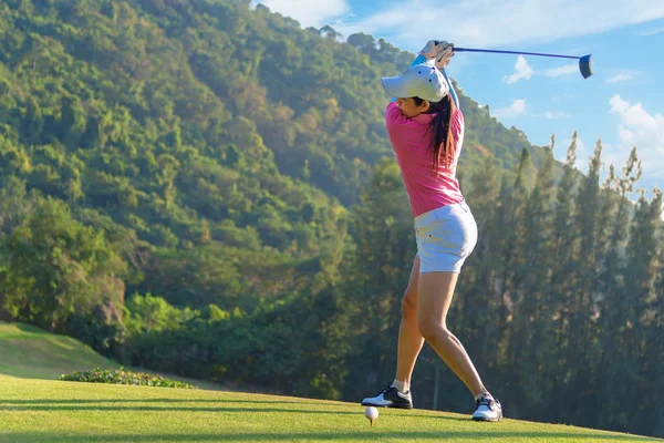 Asian woman golf player doing golf swing tee off on the green evening time, she presumably does exercise.  Healthy and Lifestyle Concept