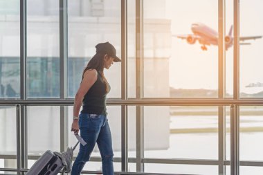 Uçak havaalanına cam pencere, kız turist tutun çanta ve bekleme salonu uçak kalkış çantamda yakınındaki bkz: Gezgin kadın planı ve sırt çantası. Seyahat kavramı