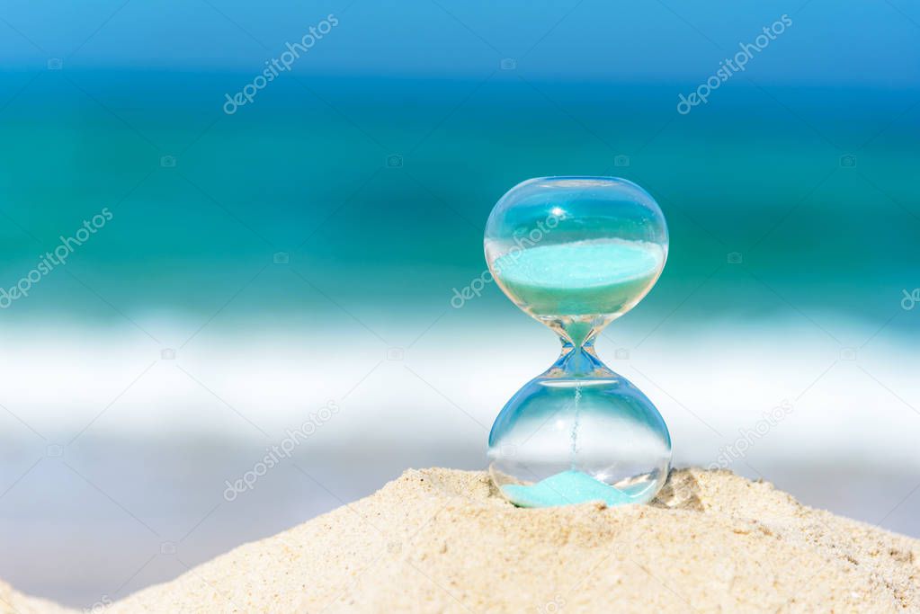 Hourglass summer and vacations time on a beach in the sand  with blue sky and copy space.  Lifestyle Concept