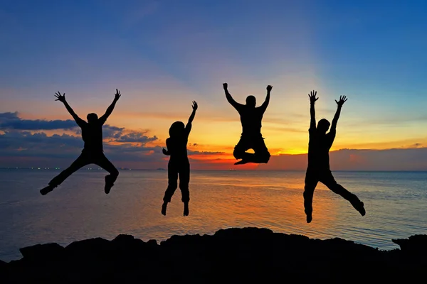 在日落的时候 朋友和团队的剪影跳跃在海滩上成功的生意 生活方式与团队合作理念 — 图库照片