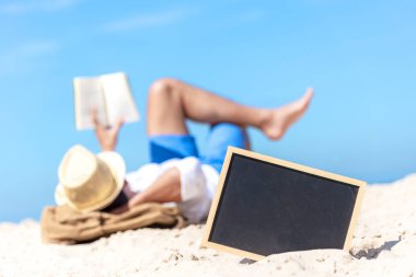 Kum Beach, arka plan beyaz turist Asya genç adam gülümseyen sakin ol mutlu bir kara tahta, kapatın ve kitap okuma. Yaz ve seyahat kavramı.