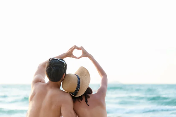 Couple in love making a heart - shape with hands on tropical on the sunset beach in holiday.  Honeymoon relax together on summer travel destination.  Valentine, Travel and Summer Concept