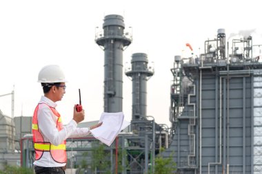 Santral enerji ve petrokimya endüstrisinde işçilerin güvenlik kontrolü için radyo ile plan tutan mühendis adam. Mühendis Kavramı