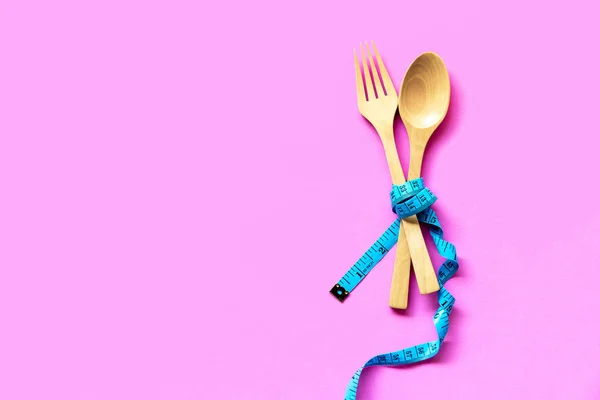 ダイエットスリミング カラフルなピンクの背景に横たわる木製のフォークの周りに巻かれた青い測定テープ ダイエットと健康的なコンセプ — ストック写真