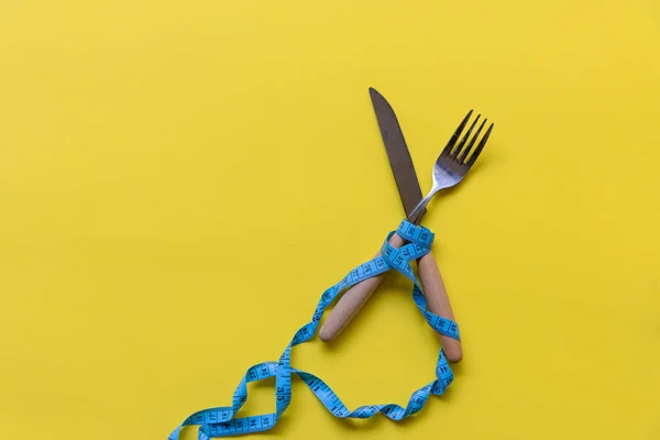 ダイエットスリミング 黄色の背景に横たわる木製のフォークの周りに巻かれた青い測定テープ ダイエットと健康的な概念 — ストック写真