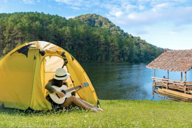 Mutlu gezgin yaşam tarzı kadınlar nehir yakınındaki ormanda gitar çalan çadırlar ile tatil kamp. Seyahat tatil Konsepti 