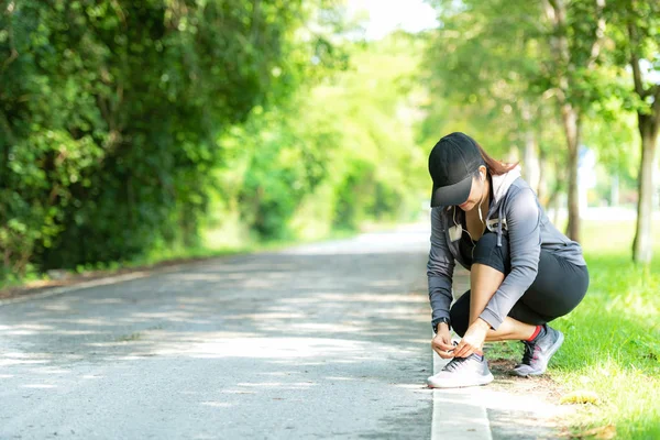 Running woman tying laces of running shoes before jogging through the road in the workout nature park.  Weight Loss and Healthy Concept