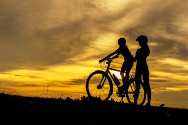 Okyanus üzerinde gün batımında Siluet bisikletçi güzel bir aile. Anne ve kızı bisiklet soğuk ve plajda dinlenmek. Yaşam Tarzı Kavramı.