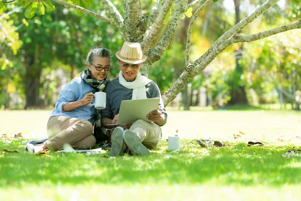 Asian Lifestyle senior couple drinking coffee and shopping online  in the nature park happy and relax time. Elderly family the rest and chill  after retirement vacations.
