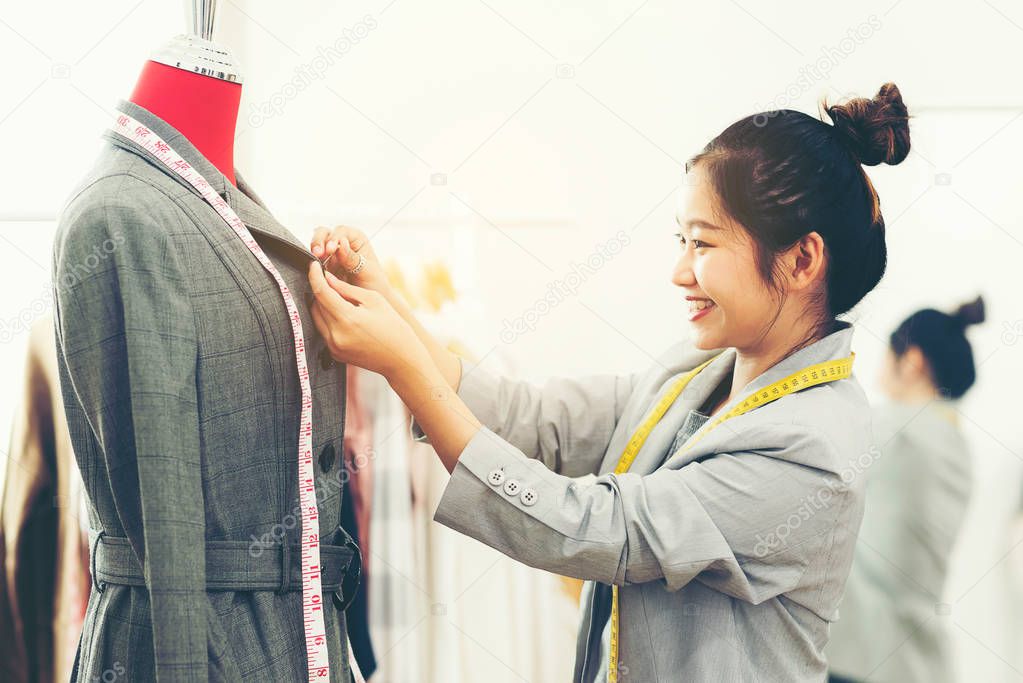 Asian young women fashion designer  working on her designer in the showroom,  Lifestyle Stylish tailor taking measurements on mannequin in studio.  Business small Concept
