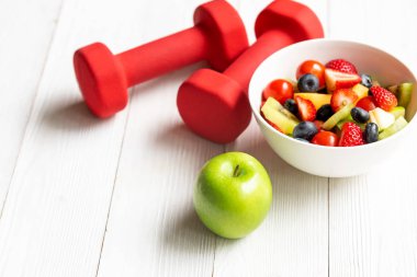 Taze meyve salatası ve halter spor ekipmanları, ahşap meyve sağlıklı yeşil elma ile kadınlar için sağlıklı yaşam tarzı diyet. Sağlıklı Konsept.