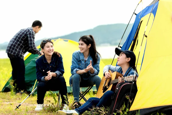 Camping outdoor. Group  friends camping leisure and destination travel. Family sitting around camp fire and playing guitar and roasted sausages, tourism relax and travel near river in holiday.