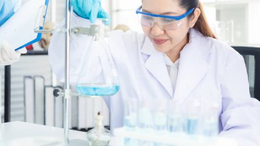 Asyalı kadın ve erkek bilim adamları virüs verilerini analiz ediyor ve atölye için mikroskop başarısını değerlendiriyor. Sağlık araştırmacıları yaşam bilimi laboratuvarında damlatan kimyasallarla ilgili bir araştırma yapıyor..