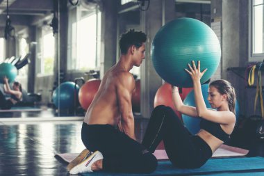 Yoga topunu eğiten antrenör, spor salonunda bir kadınla vücut zayıflığı ve sağlıklı bakımı için egzersiz yapıyor. Beden eğitimi eğitmeni müşterileriyle spor yapıyor. Sağlıklı Spor Konsepti
