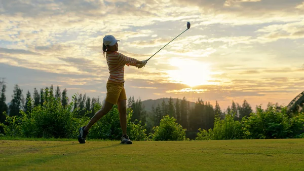 Golfer sport course golf ball fairway.  People lifestyle woman playing game golf tee of on the green grass sunset background.  Asia female player game shot in summer. Healthy and Sport outdoor