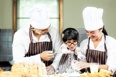 Yemek pişiren aile. Şef anne ve çocuk tost pişiriyor ve akşam yemeği için ekmek yapıyorlar. Asyalı oğul anneye tatlı yemek yapmada yardım ediyor, çok mutlu ve keyifli. Aile Yaşam Tarzı Konsepti
