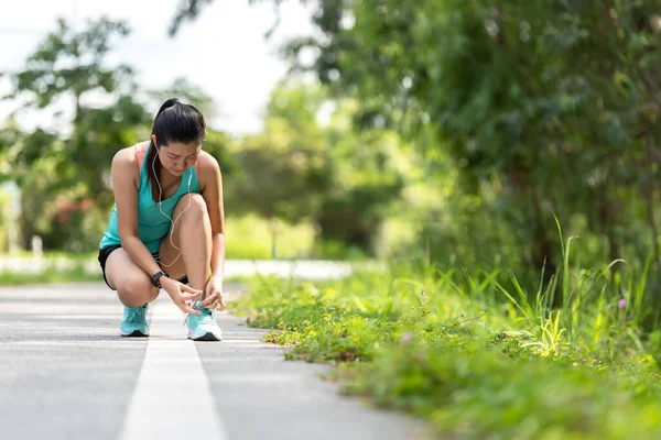 Koşucu genç Asyalı kadın spor parkında koşmadan önce spor ayakkabısı bağcıklarını bağlıyor. Kilo Verme ve Sağlıklı Konsept
