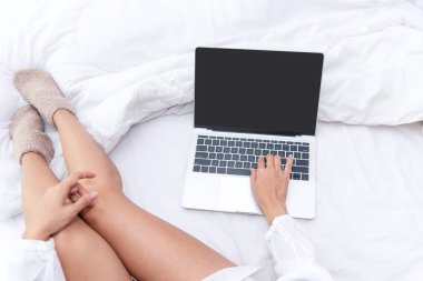 Bacaklarını kapat. Yatak odasındaki beyaz yatakta yatan kadınlar. Sabahları dizüstü bilgisayarda çalışan kadınlar kış mevsiminde rahatlarlar. Yaşam Tarzı Konsepti.